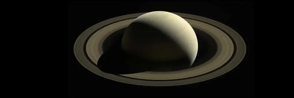 Saturn is a pale yellow in this image, with its stunning rings made of ice and rock fragments clearly visible, casting delicate shadows.