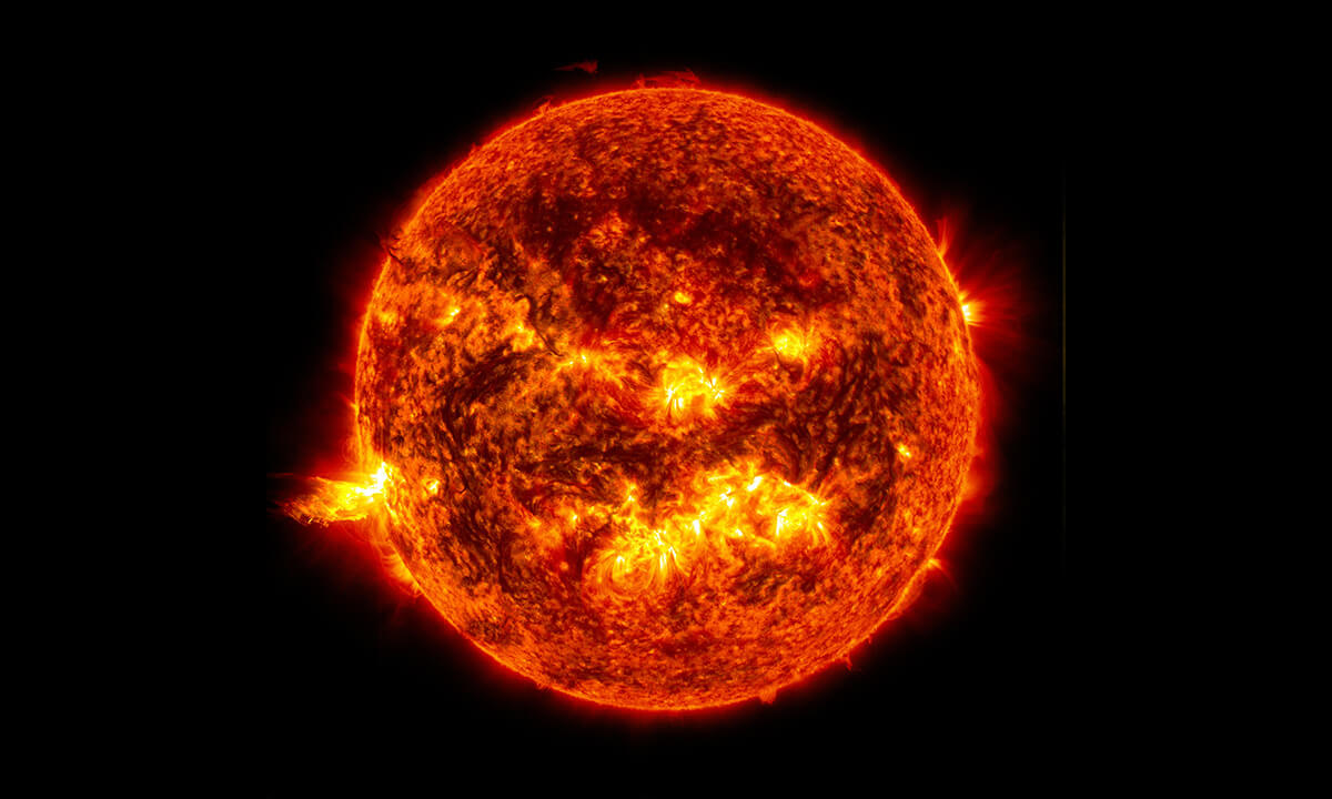 The Sun glows golden yellow in this image, its surface alive with swirling patterns of plasma and dark sunspots. Bright flares shoot outward from its edges.